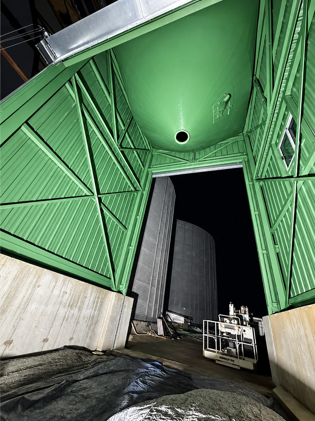 Structure métallique peinte en vert clair, éclairée de nuit, ouvrant sur une cellule galvanisée dans l’ombre.