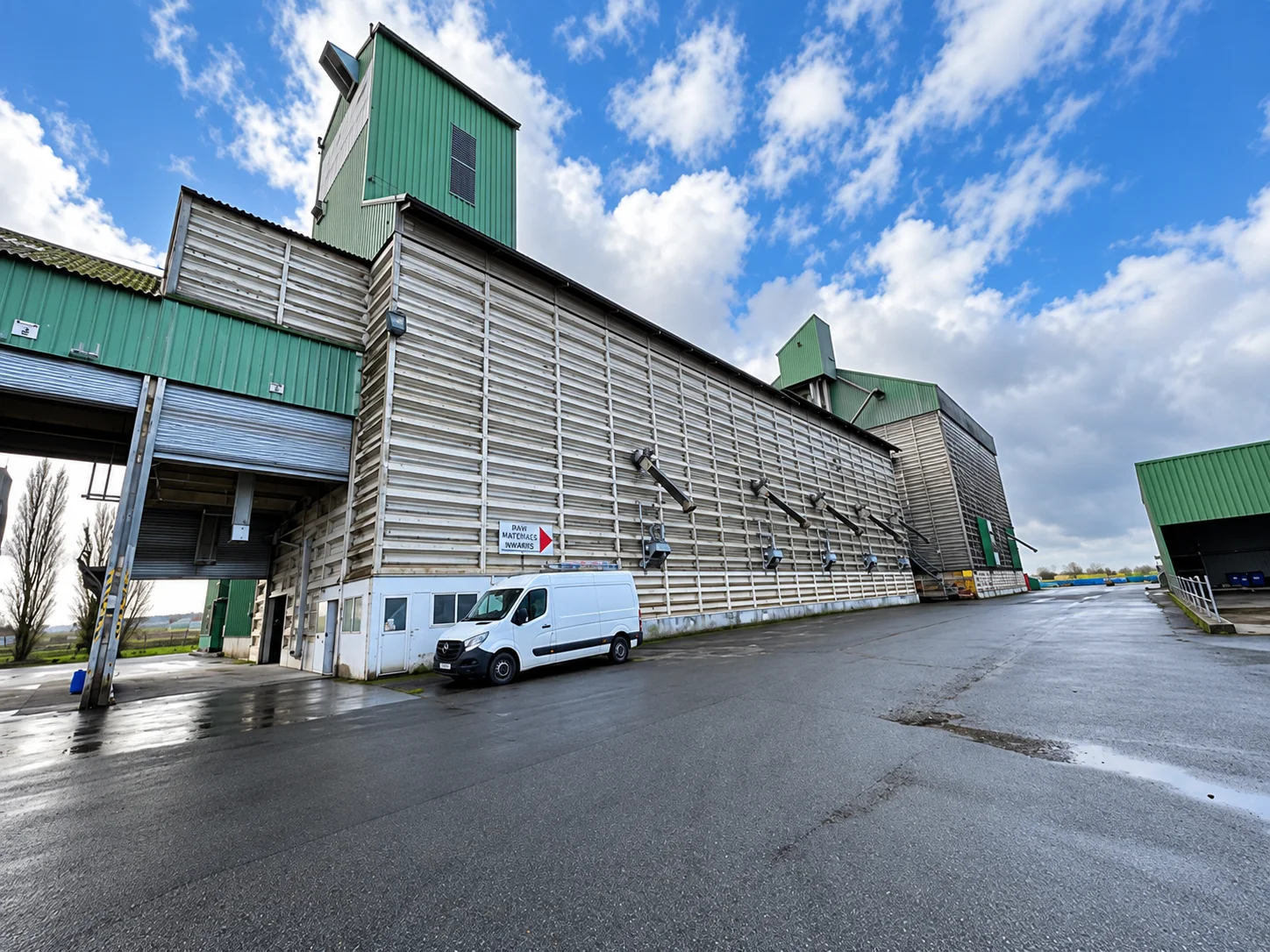 Site de stockage non traité, bardage délavé, fourgon d’intervention au pied du bâtiment, sol mouillé.